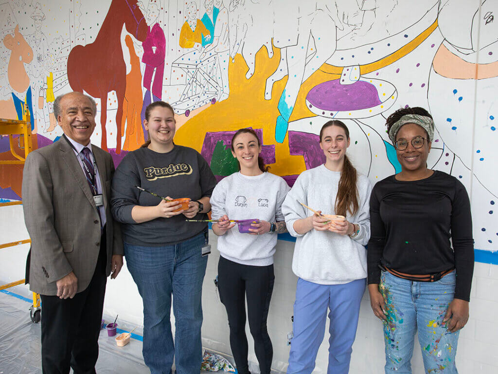 Dean Reed, Tia Richardson, and students pose in front of the mural in progress