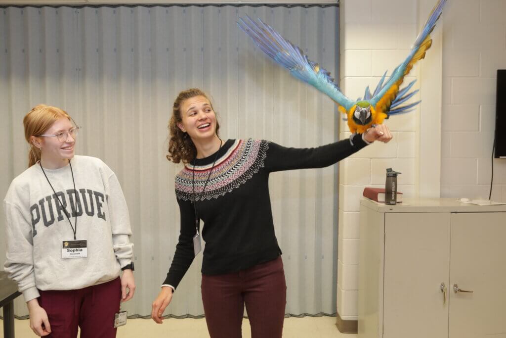 Purdue Veterinary Nursing student Sophia Minnerath, of the Class of 2027, and Purdue Small Animal Medicine and Surgery Intern Rachel Illgen, get up close and personal with a Parrot at the Purdue MMAS Symposium in Lynn Hall.