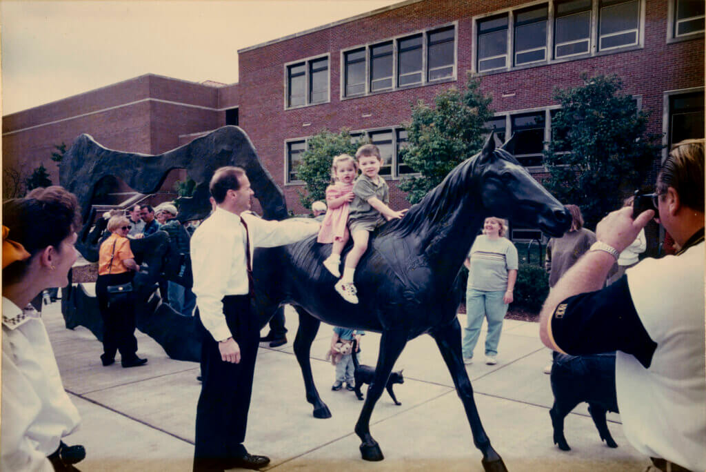 Bret Marsh looks on as his children, Spencer and Lacey, enjoy being the first to sit on the horse after the dedication of the Continuum Sculpture by Larry Anderson in 2000.