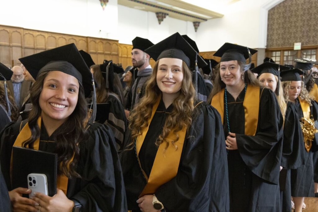 Veterinary school graduates smiling at the camera as they walk through the Purdue Memorial Union Ballroom