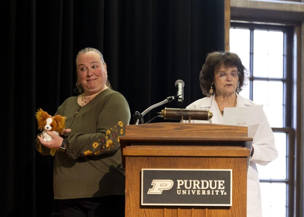 Instructional Technologist Jeannine Henry displays a Papillon stuffed animal as Dr. Joanne Messick reads their poem, “The Gift of the Papillon,” that they wrote for the ceremony.