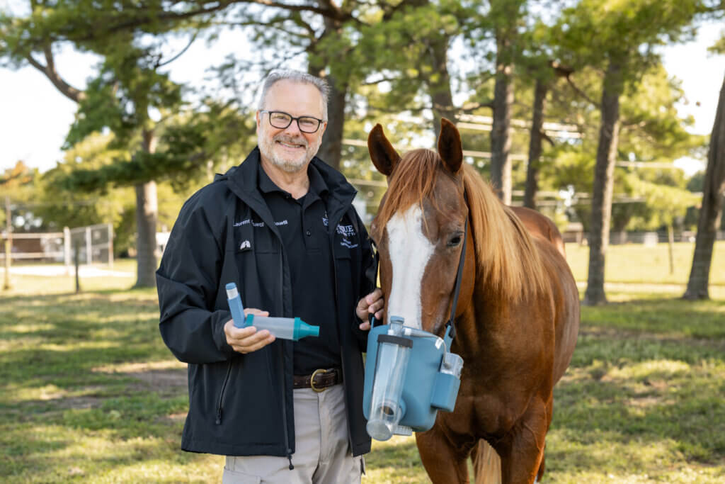Man holding a medical device and standing next to a horse