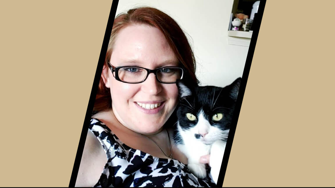 A female is featured prominently next to a black and white cat. The woman is wearing glasses and has red hair, and is smiling at the camera.