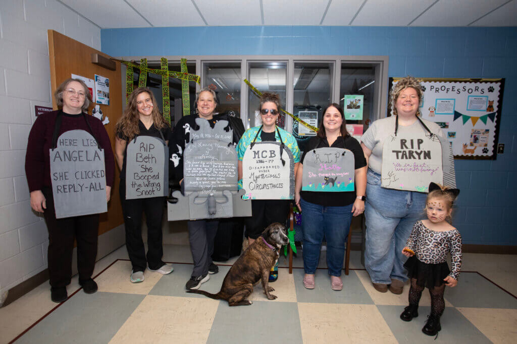 Tombstone-shaped signs explained the “reasons” for the supposed demise of several Veterinary Technology Program Office staff members: (left-right) Angela Arellano, Beth Laffoon, Holly McCalip, Molly Cripe Birt, Holly Englert, and Taryn Adams, who was joined by her daughter Monroe.