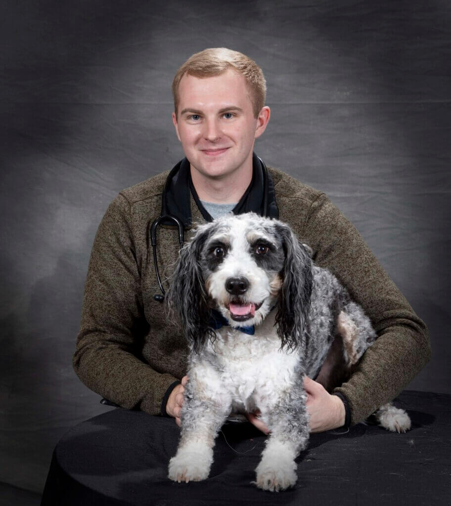 portrait of a young man with short blonde hair posed with his gray and white dog in front of a dark gray background
