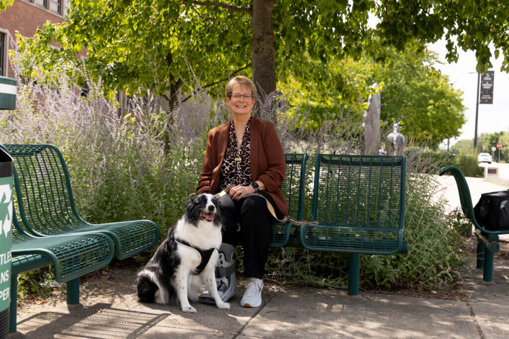 woman sitting outdoors under a tree on a bench with her dog sitting next to her