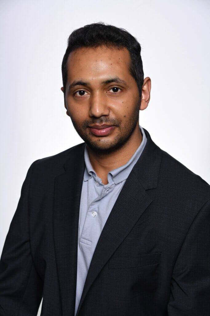 portrait of a man wearing a dark suit jacket and a blue button up shirt. The portrait has a white background