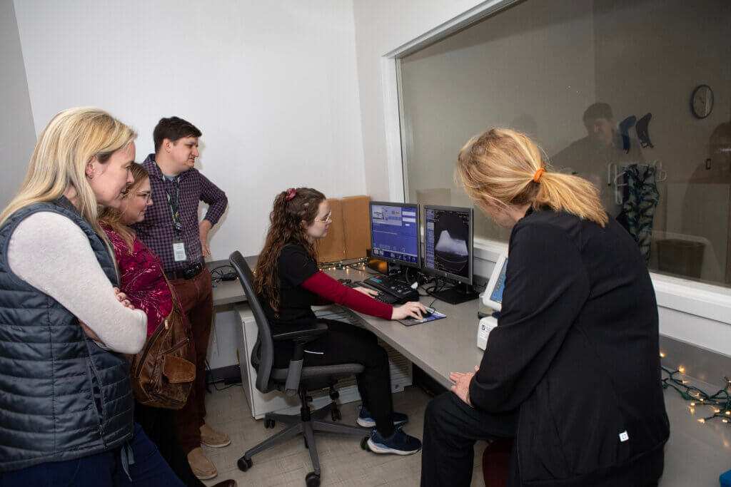 A group of people standing around a computer, with one person sitting in front of the screen. The group is reviewing the results of the CT scan of the fossil.