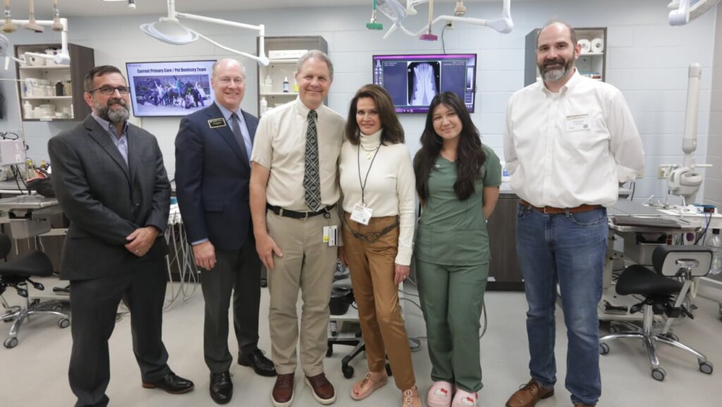 A group of six people stand for a photo in front of veterinary dental equipment