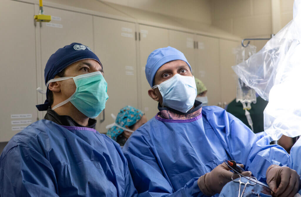 Two medical professionals wearing scrubs are working side by side. They are both focused, facing the camera.