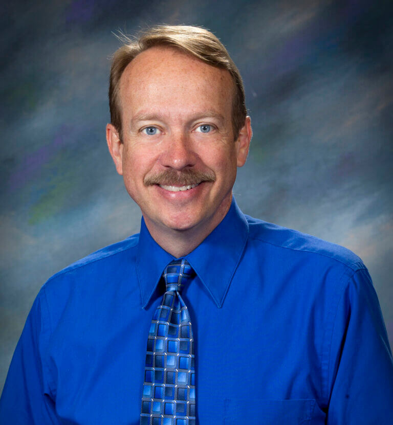 portrait of man in a bright blue shirt in front of a dark gray background