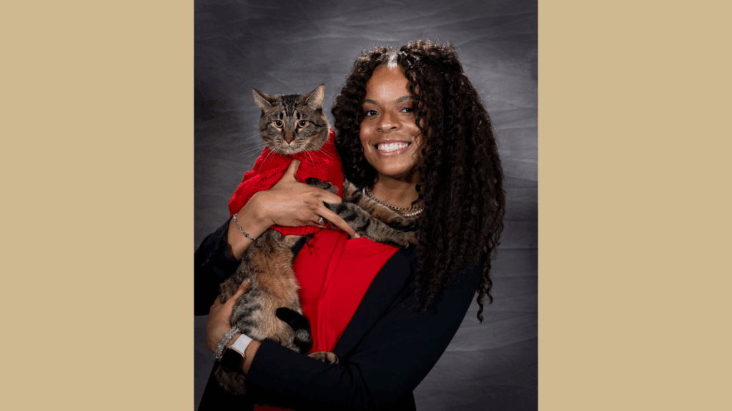 portrait of a young woman with long, curly, dark hair wearing a red shirt. She is holding a cat that is also wearing a red shirt.