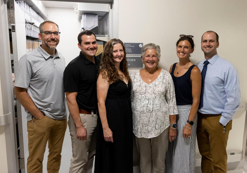 A group of six people in casual attire standing in front of a wall