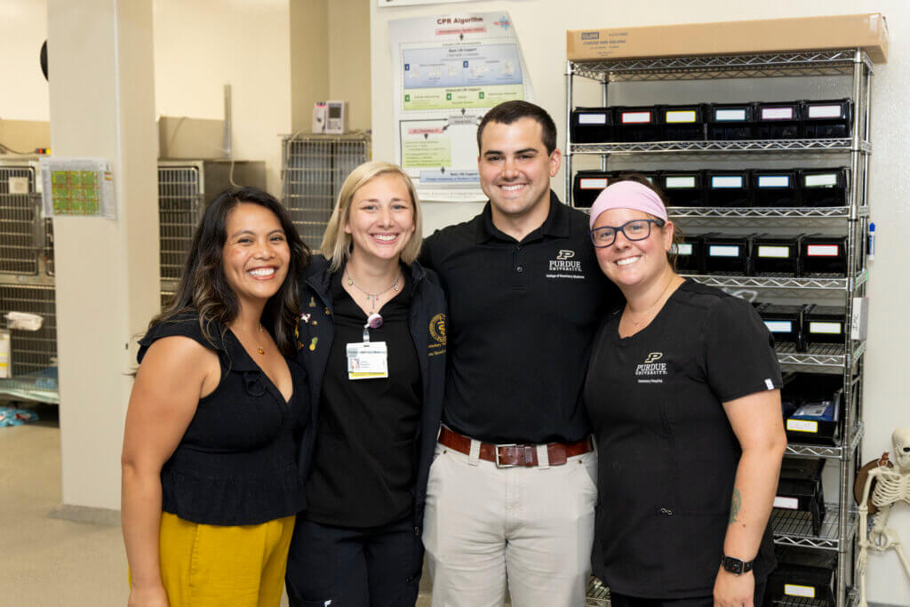 Three women and one man stand together in front of a veterinary setting, all dressed in black clothes