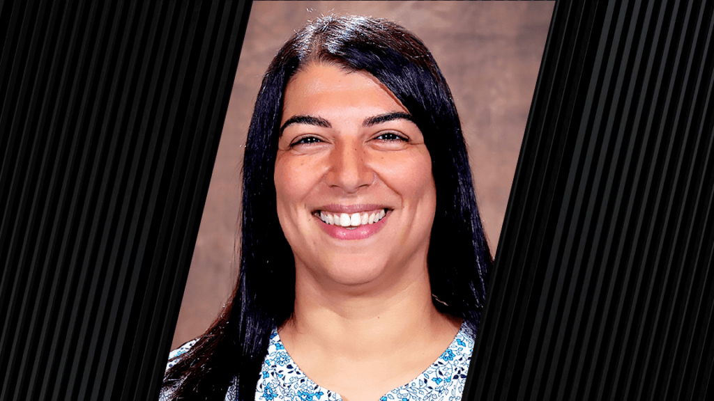 woman with long dark hair, wearing a white shirt that has a blue floral print