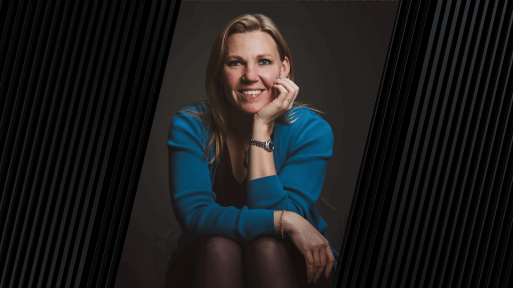woman with blonde hair posed for a photo, smiling and wearing a long sleeve blue shirt and wrist watch