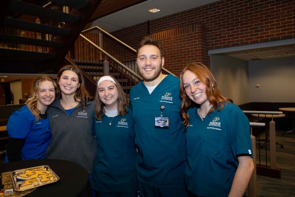 A group of young adults stand smiling, wearing blue clothes.