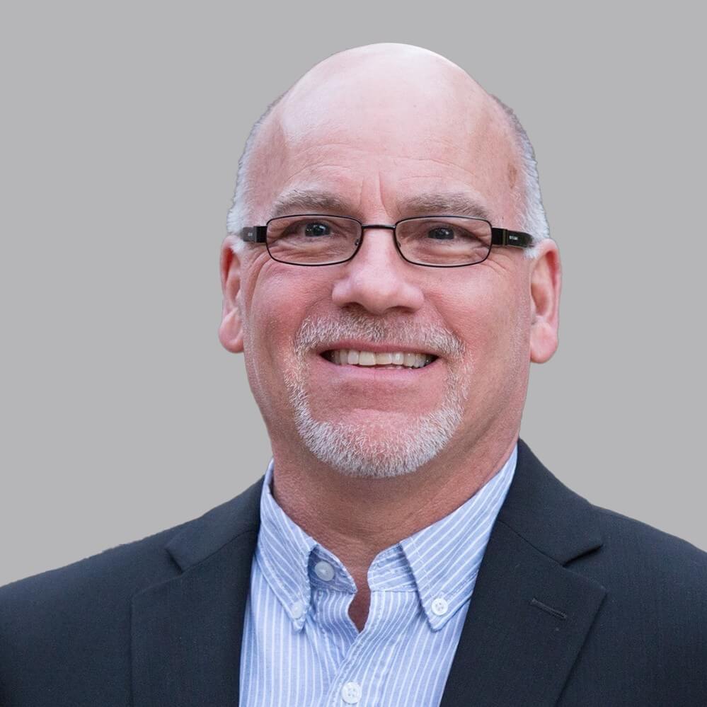portrait of a man wearing glasses, a blue dress shirt, and dark suit jacket