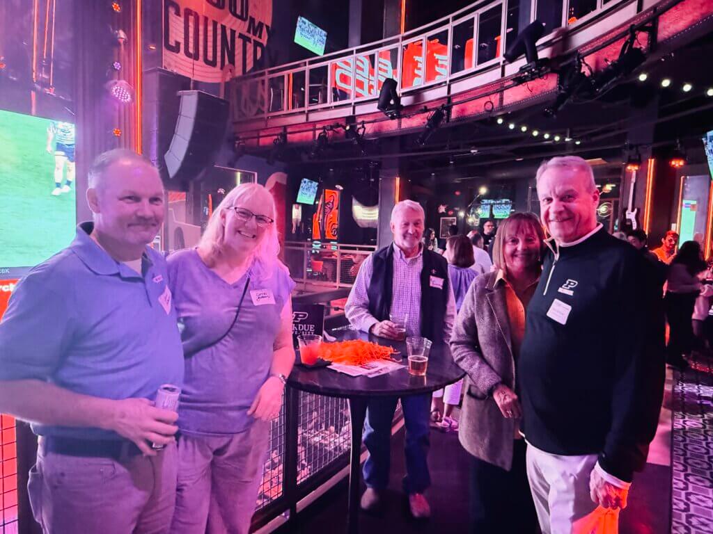 A group of five people are posed around a reception table in a room that has a pink neon-glow