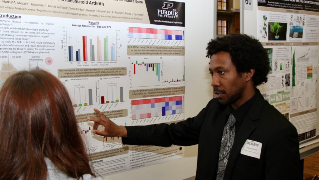 A man wearing a black shirt is presenting a research poster to a woman