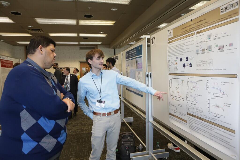 A man in a blue dress shirt is presenting research to a man in a blue sweater