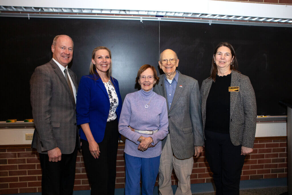 A group of five people stand in front of a chalkboard and are dressed in formal attire.