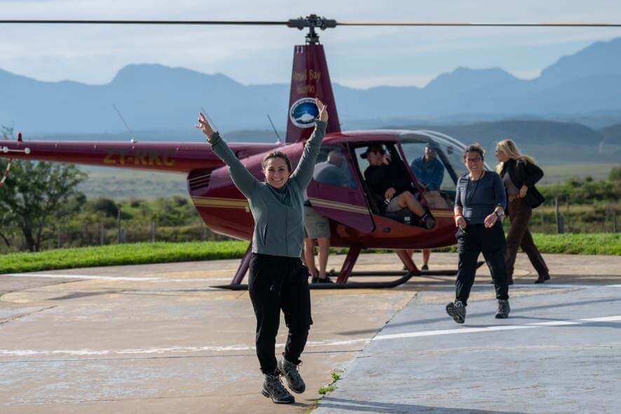 A female is featured in the image posing with her arms in the air and is standing in front of a red helicopter