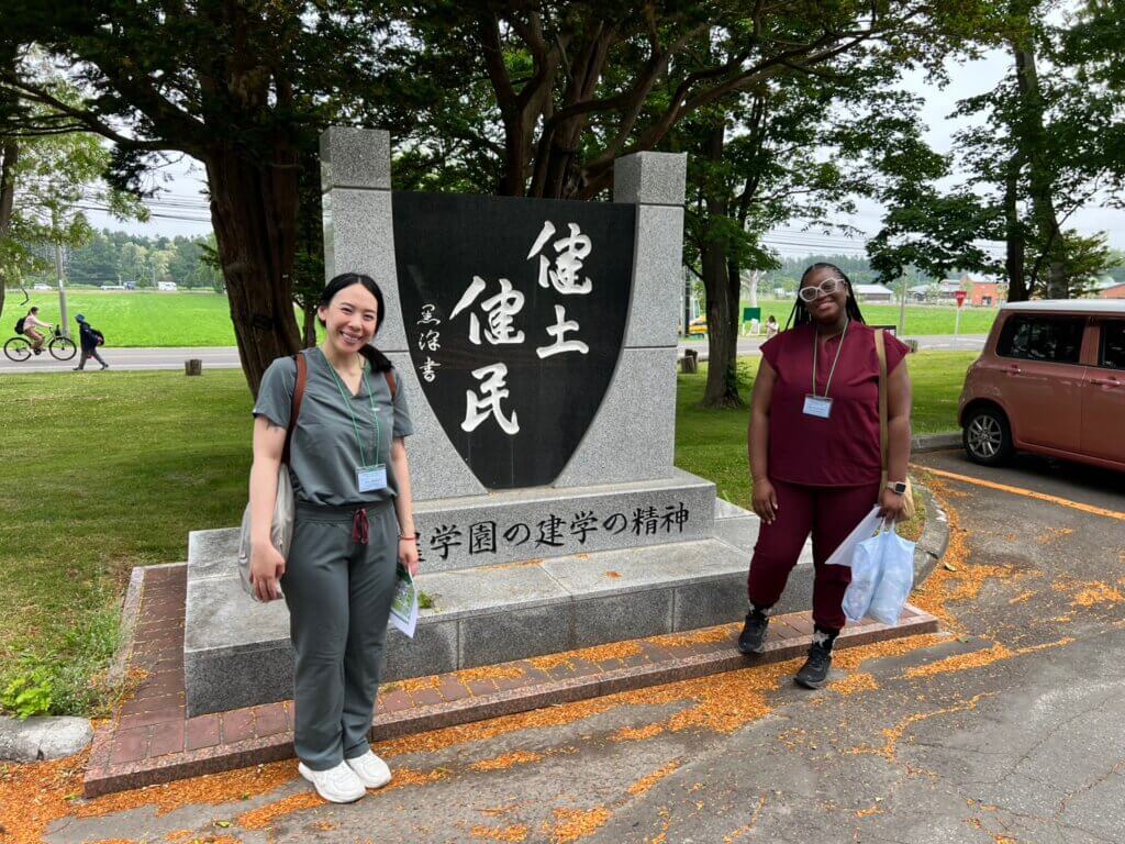 Two females stand on either side of a stone sculpture with oriental characters inscribed on it