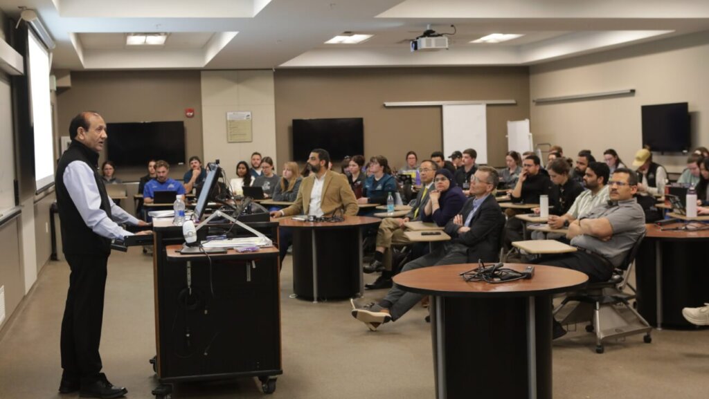 A man is standing in front of an attentive audience and is giving a presentation of some kind behind a podium