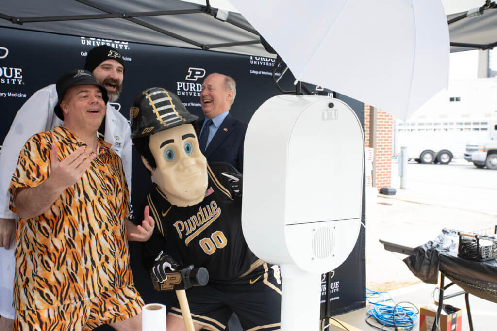 four figures, including the Purdue University mascot are posed for a photo at a Photo Booth station