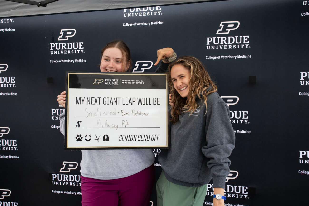 Two females are standing in front of a Purdue University-themed backdrop and are holding a sign that says "My Next Giant Leap Will Be Small animal and Exotic Practitioner at McMurray, PA"
