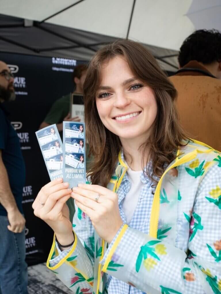 A female wearing a white and green jacket is holding up Photo Booth printouts