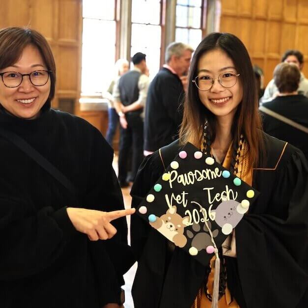 Two females are interacting with a graduation cap that reads "Pawsome Vet Tech 2026"