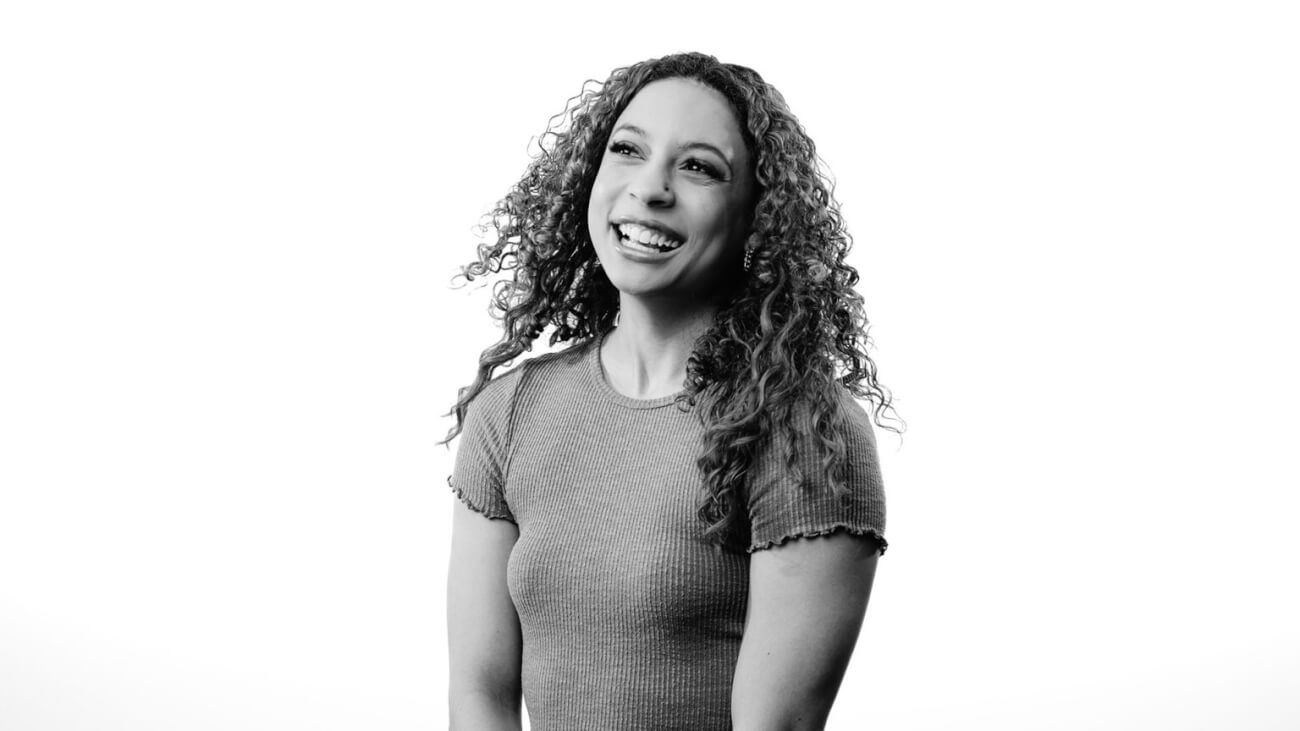 black and white portrait of a woman with long curly hair, looking away from the camera and smiling