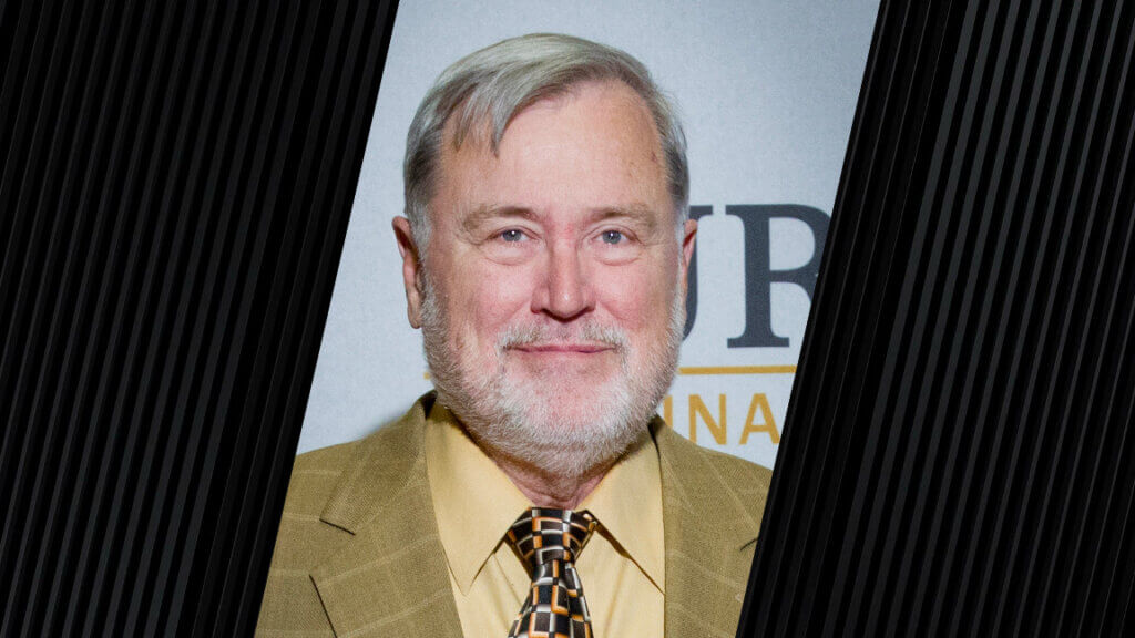 a portrait of a man who is wearing a yellow-green, plaid suit jacket, and a square-pattern tie