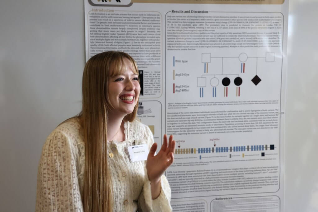 A woman is standing in front of a science research poster, appearing to be in a cheerful conversation with an out-of-frame figure.