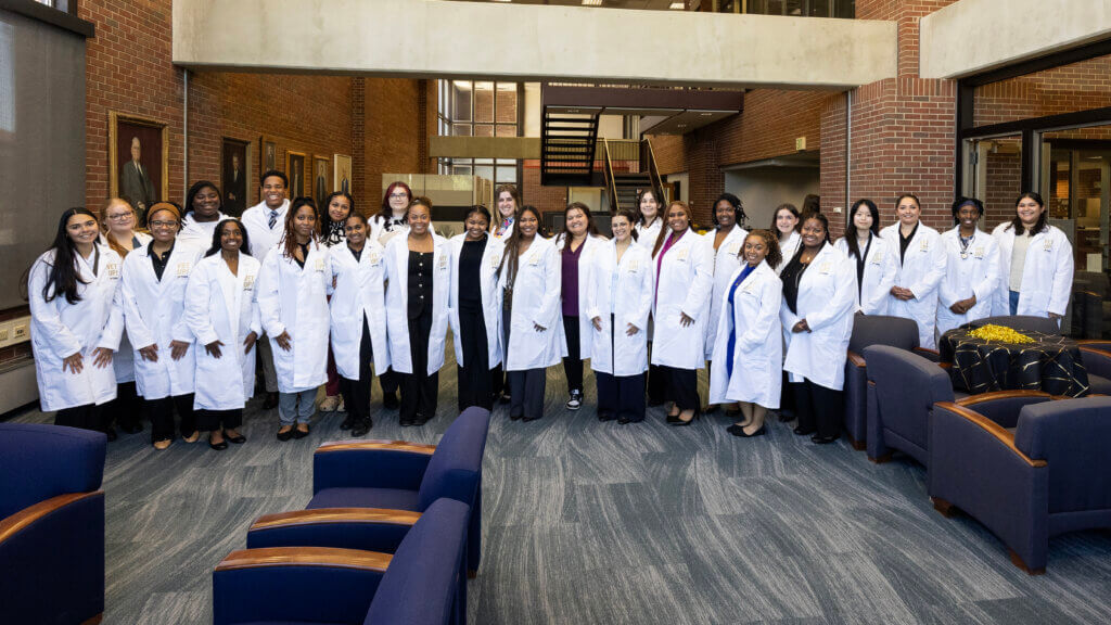 Several people are wearing white coats in a large, carpeted, brick room.