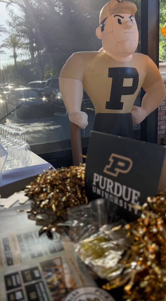 An inflatable Purdue University mascot is sitting on a table surrounded by gold and black items