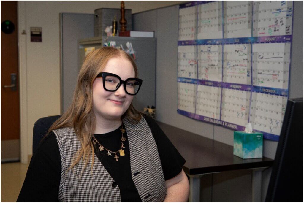 A female in an office setting is wearing glasses and a vest