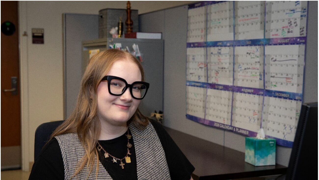 A female in an office setting is wearing glasses and a vest