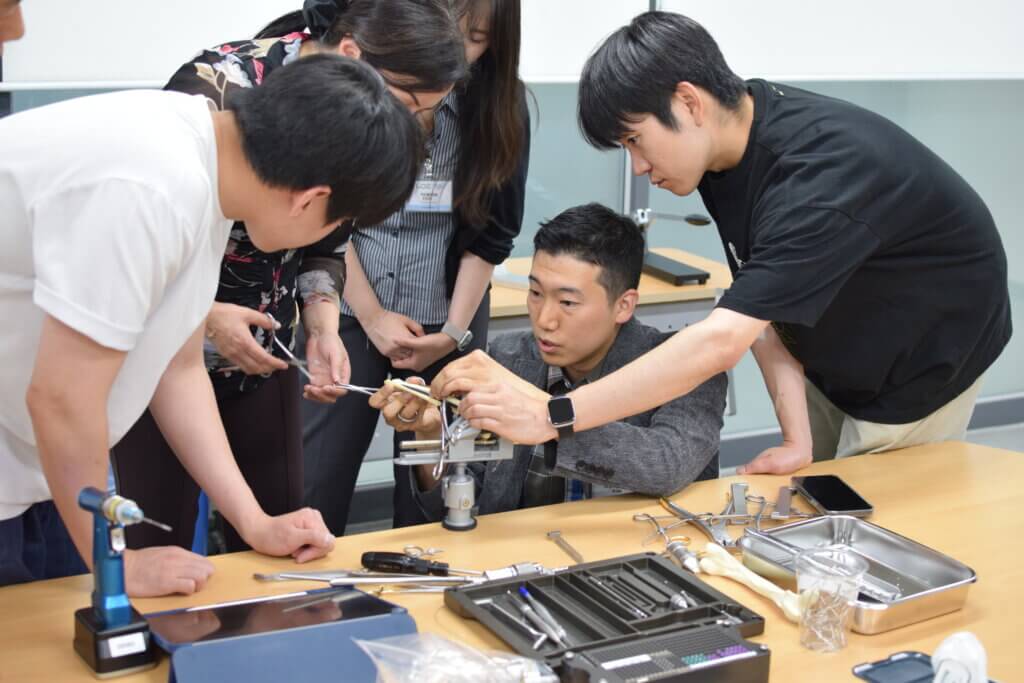 people are observing a hands on anatomy demonstration, positioned at a table. Some people are standing and others are crouching. 