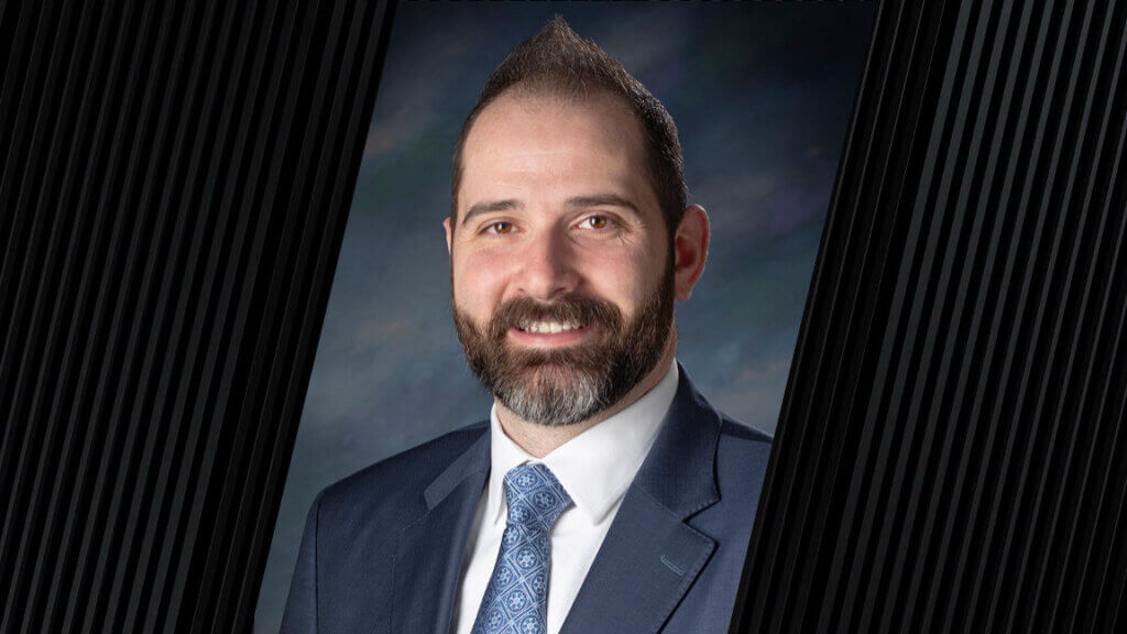 portrait of a man wearing a blue tie, white shirt, and gray jacket