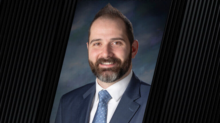 portrait of a man wearing a blue tie, white shirt, and gray jacket