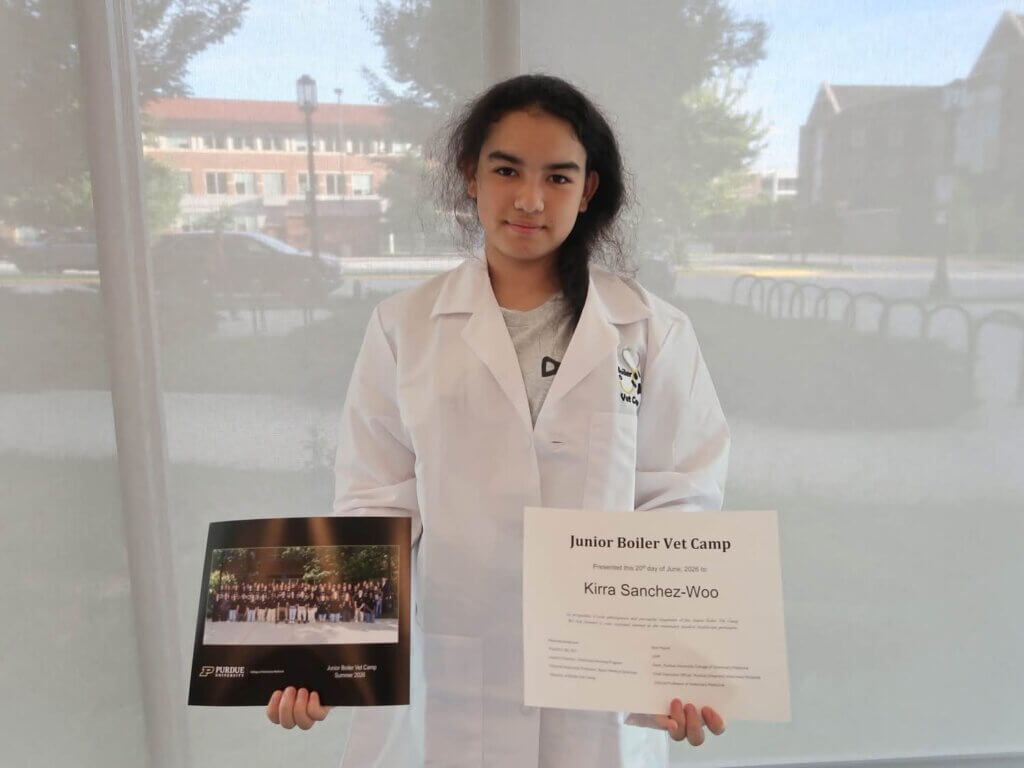 A person is wearing a white coat, and is holding a photograph on the left side of the photo, and a certificate on the right side of the photo.