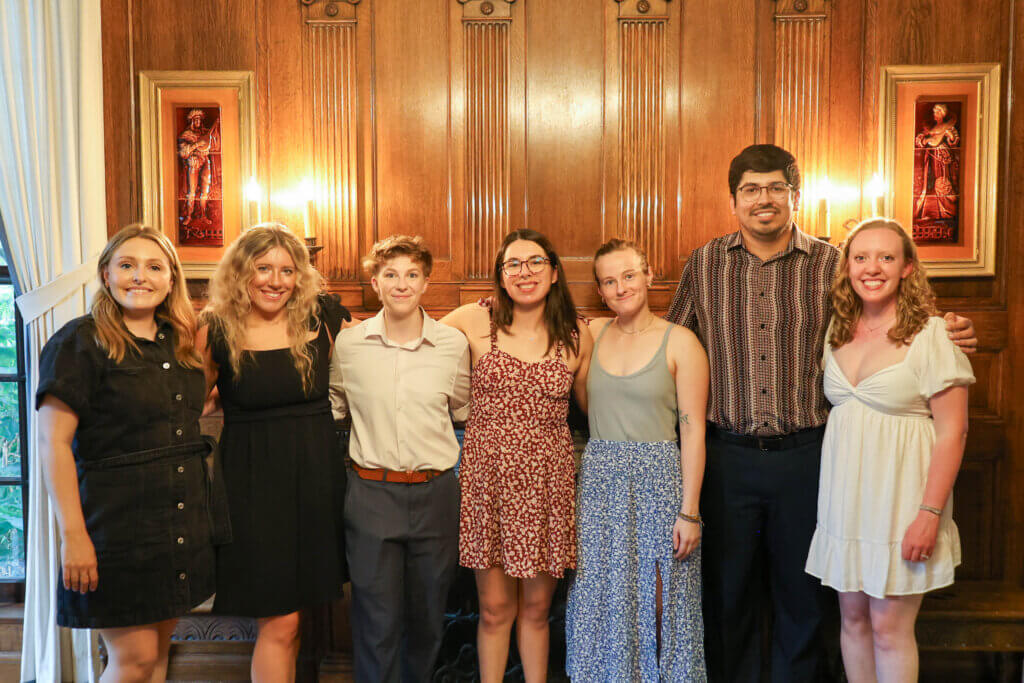 A group of people stand side by side in a dimly lit, formal setting