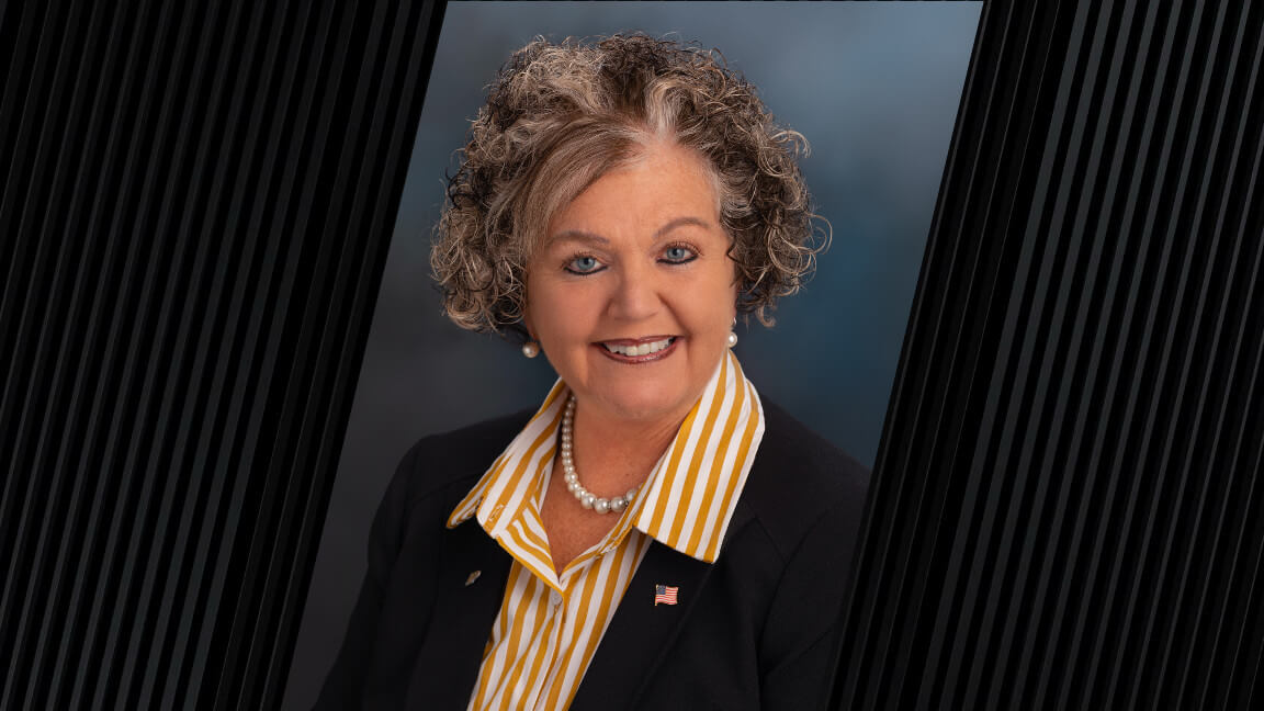 portrait of a woman with curly hair, wearing a striped yellow and white shirt and a black jacket with an American flag pin