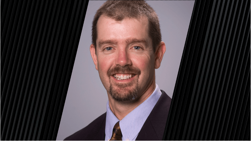 portrait of a man wearing a violet shirt, a reflective tie, and a dark jacket