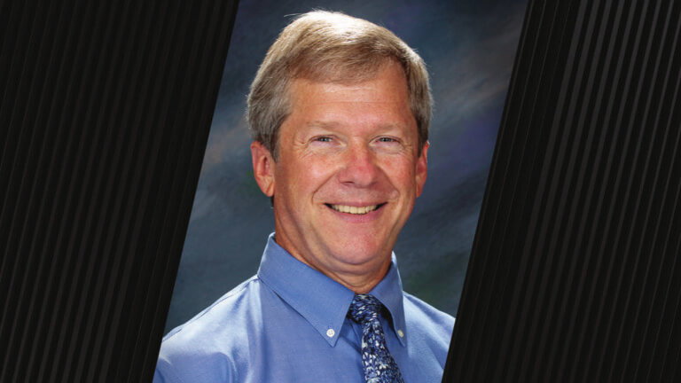 portrait of a man wearing a blue button up shirt and a blue floral-pattern tie
