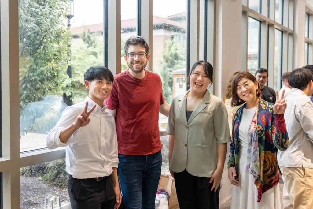 A group of four people are standing in front of a window, all appearing happy and smiling.