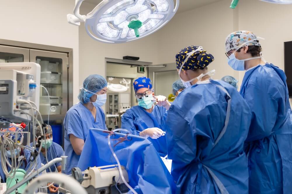 A surgical team is pictured in a medical room. All four featured people are wearing scrubs and personal protective equipment.